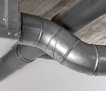 Close-up view of interconnected metal air ducts with visible seams, mounted on a ceiling. The ducts are slightly angled, showcasing their industrial appearance and functionality for ventilation purposes. This intricate setup exemplifies top-tier HVAC services in Los Angeles County, CA.