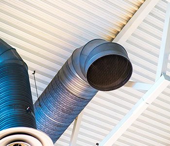 A large metal ventilation duct extends from a corrugated white ceiling, curving downward. The shiny, ribbed ducts are supported by white beams and suggest an industrial or commercial space. Expertly installed, this setup showcases top-tier HVAC services in Los Angeles County, CA.