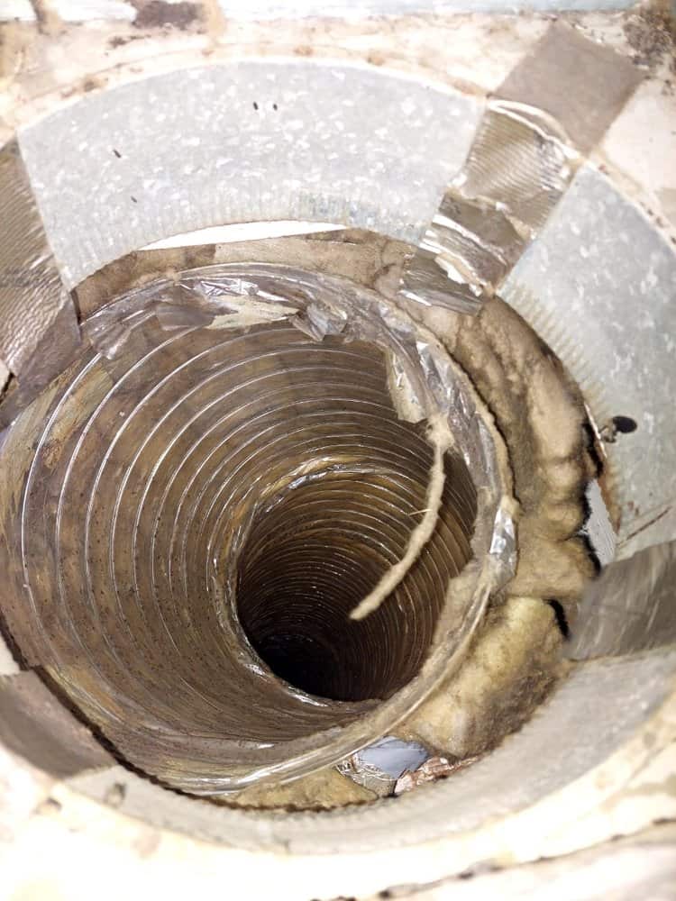 Close-up view of a damaged duct with torn insulation and loose wires. The metal interior of the duct is visible, and the surrounding insulation appears worn and frayed. Duct tape is haphazardly applied around the edges.