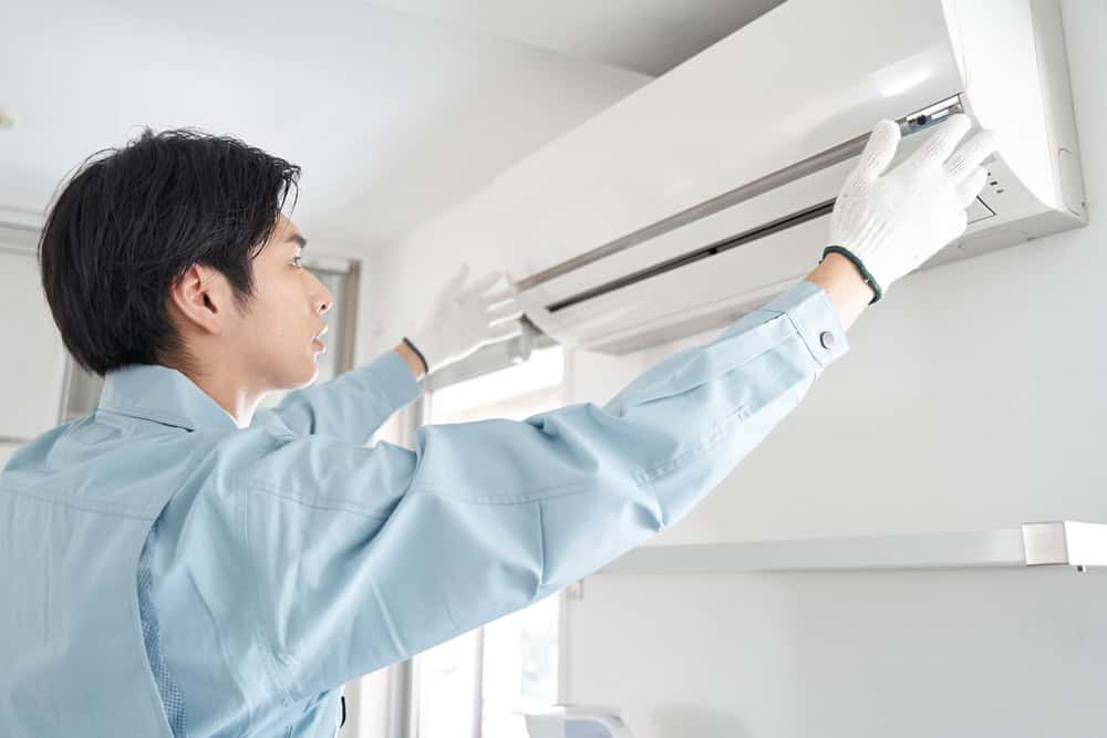 A person in a light blue uniform and white gloves is meticulously inspecting a wall-mounted air conditioner in a bright room, showcasing the expertise of HVAC services in Los Angeles County, CA. The focus remains on the individual and the air conditioning unit.